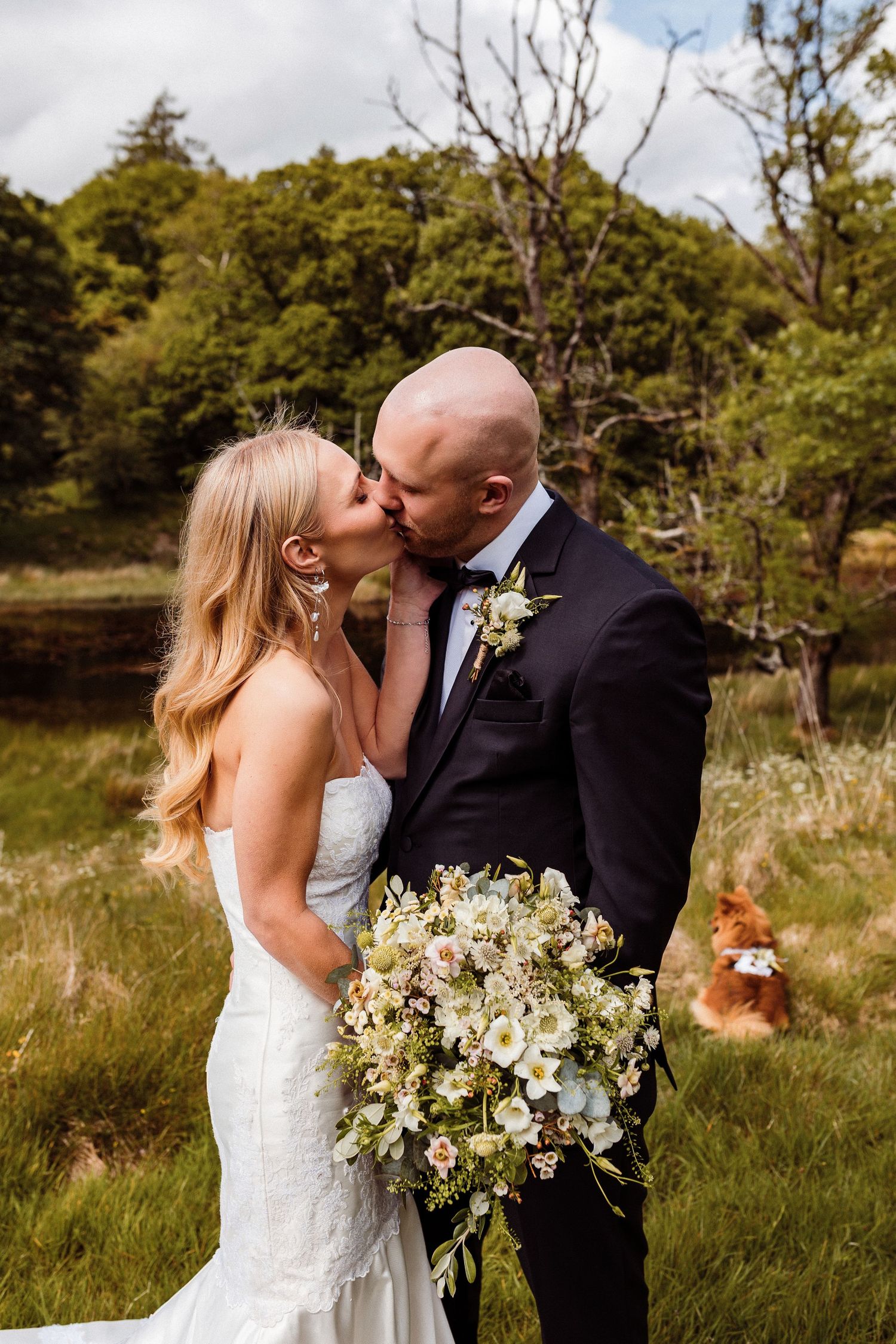 A romantic wedding couple shares intimate moments in a natural outdoor setting with lush greenery and wildflowers.