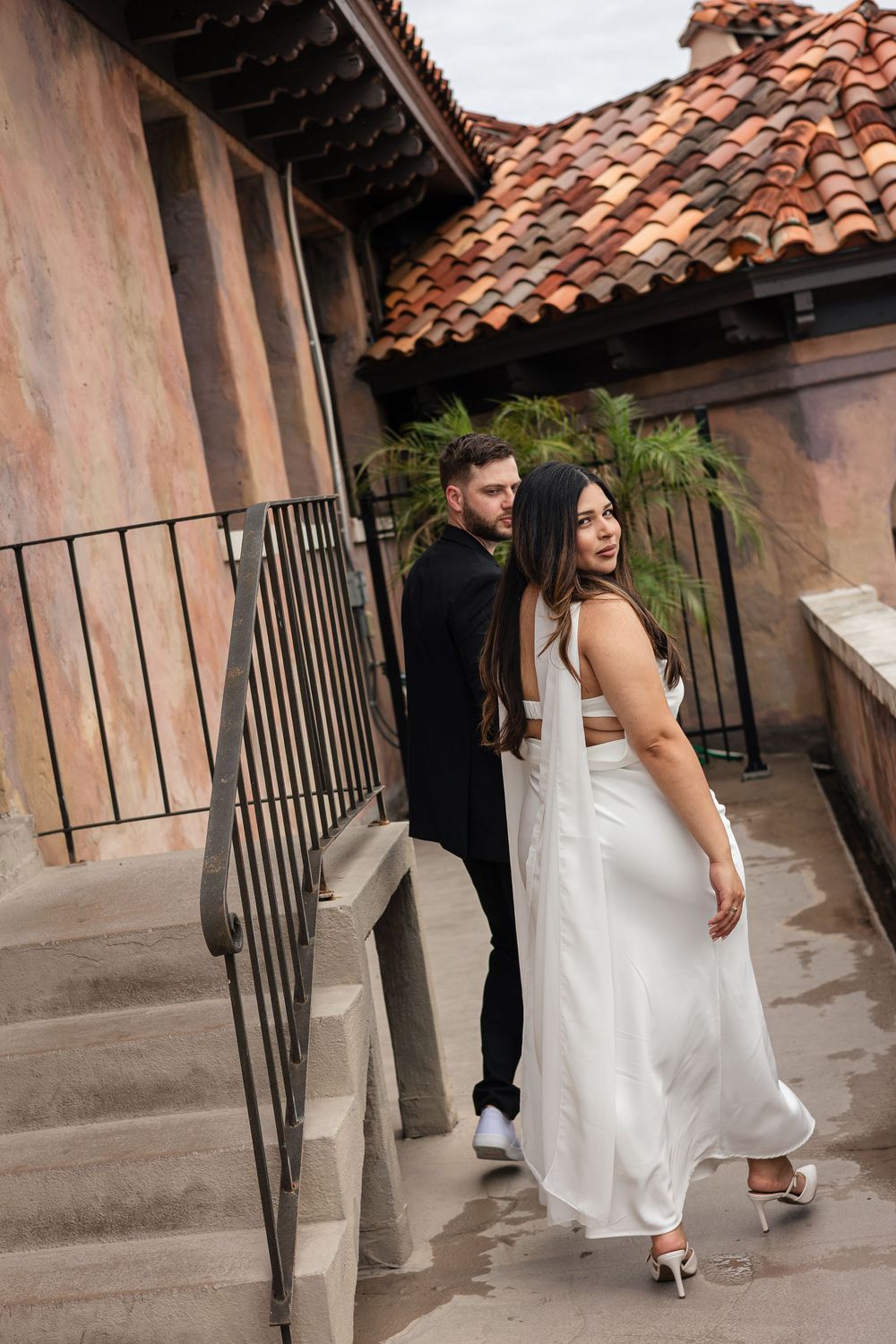 A sequence showing a couple walking along a Spanish-style building exterior with terracotta roof tiles.