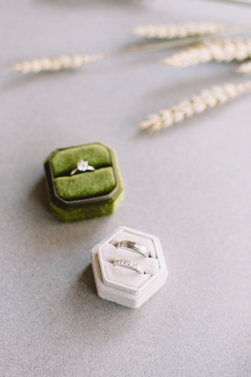 A collection of small hexagonal ring boxes in green velvet and white, arranged in a horizontal progression on a gray surface.