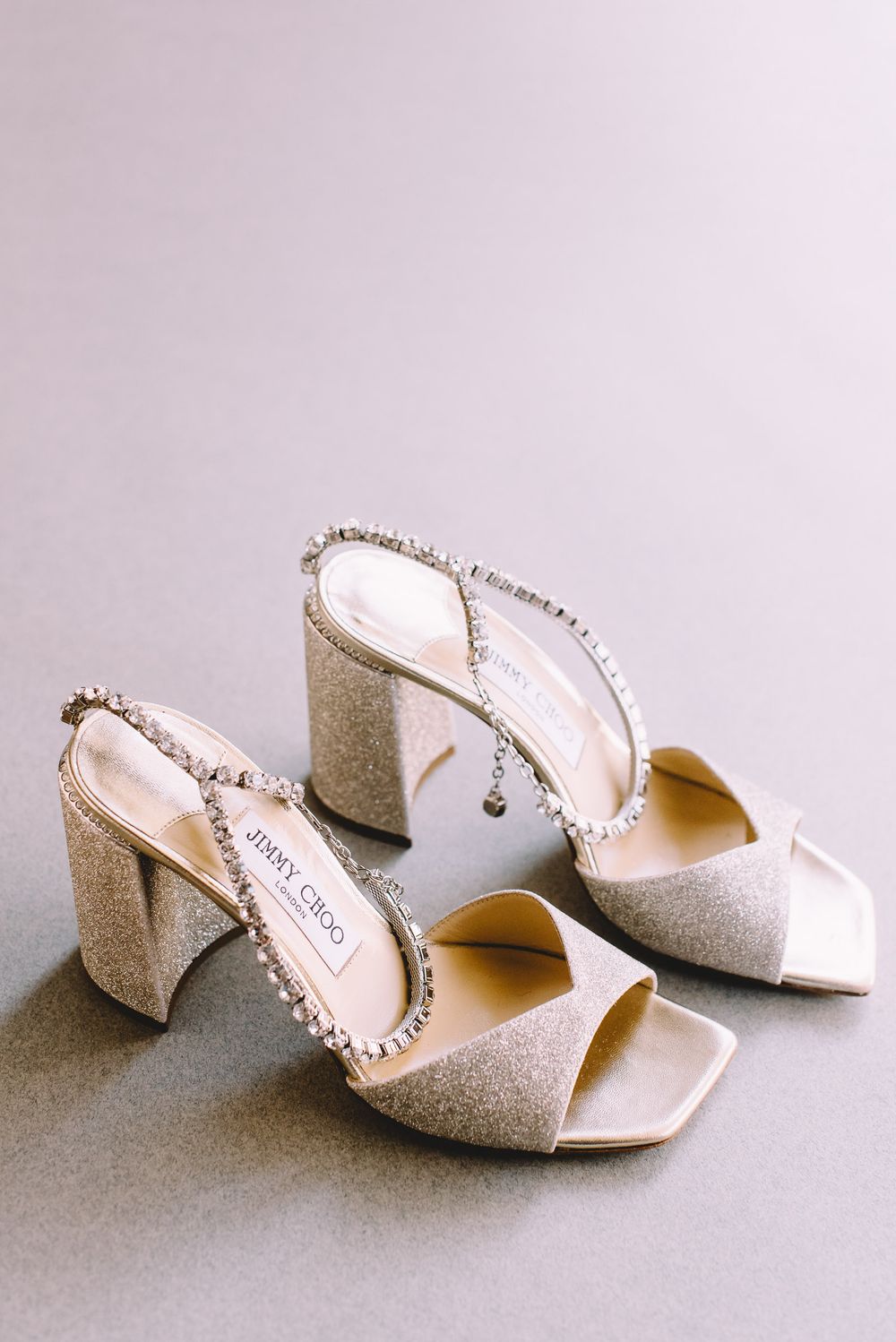 Four elegant white glitter bridal mules with block heels arranged in a row showing different angles on a neutral surface.