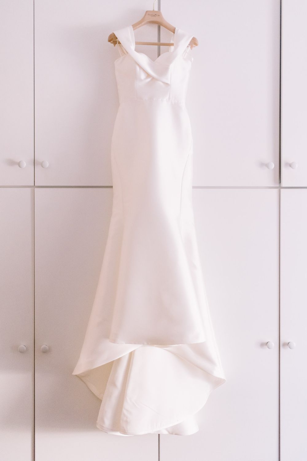 Elegant white wedding dress with mermaid silhouette hanging on display against white closet doors.