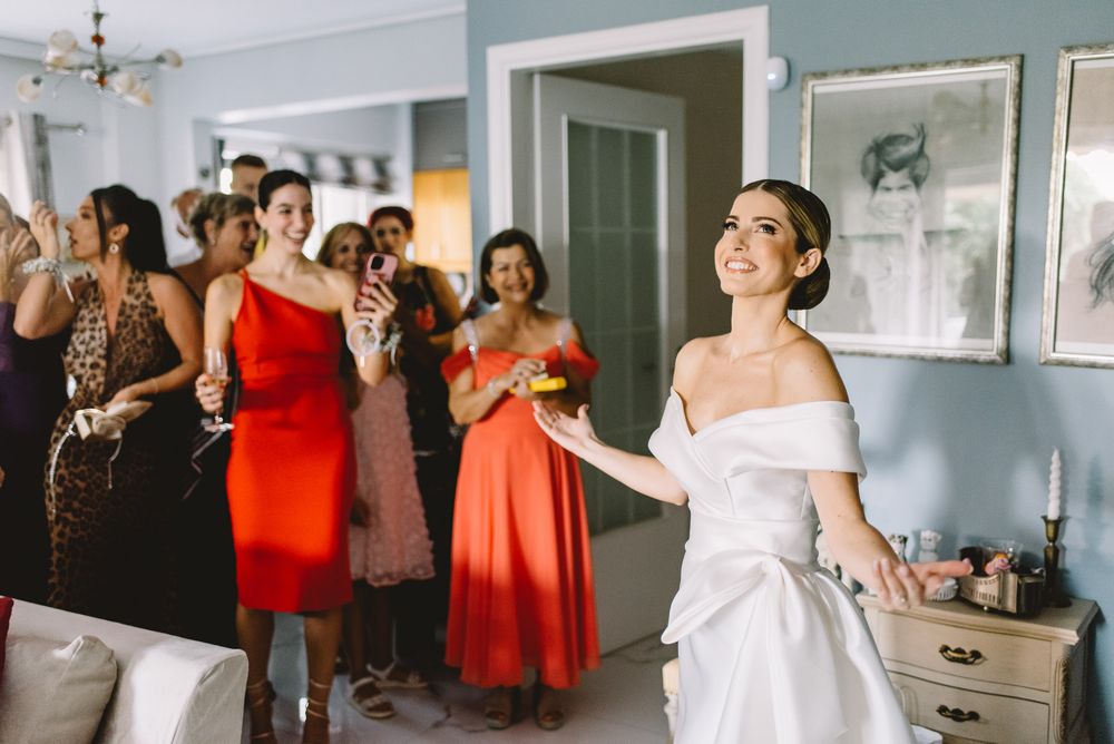 Group getting ready in a sunlit dressing room wearing coral and peach colored bridesmaid dresses on a wedding day.