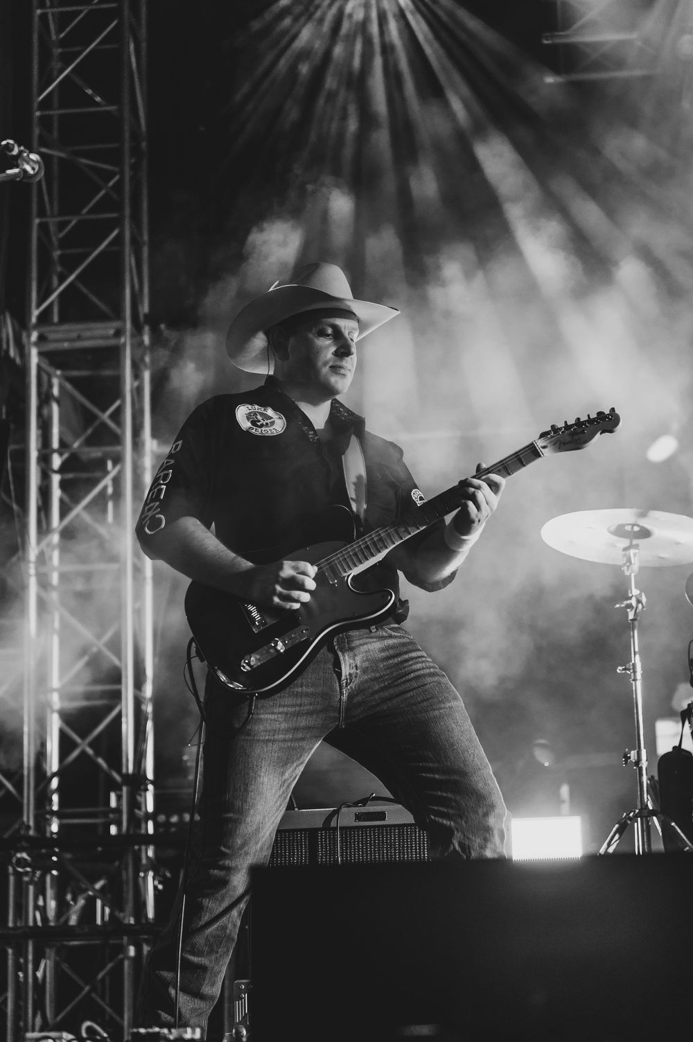 Black and white photo of a guitarist in cowboy hat performing on stage with dramatic lighting and smoke effects.