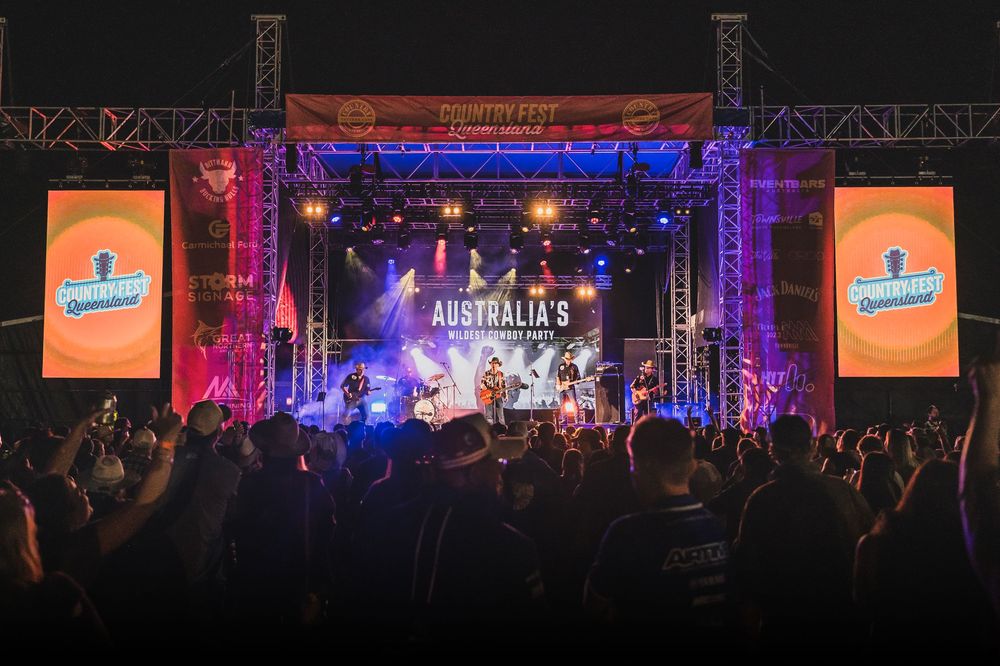 Outdoor country music festival stage with colorful lights, live band, and large crowd at night in Australia.