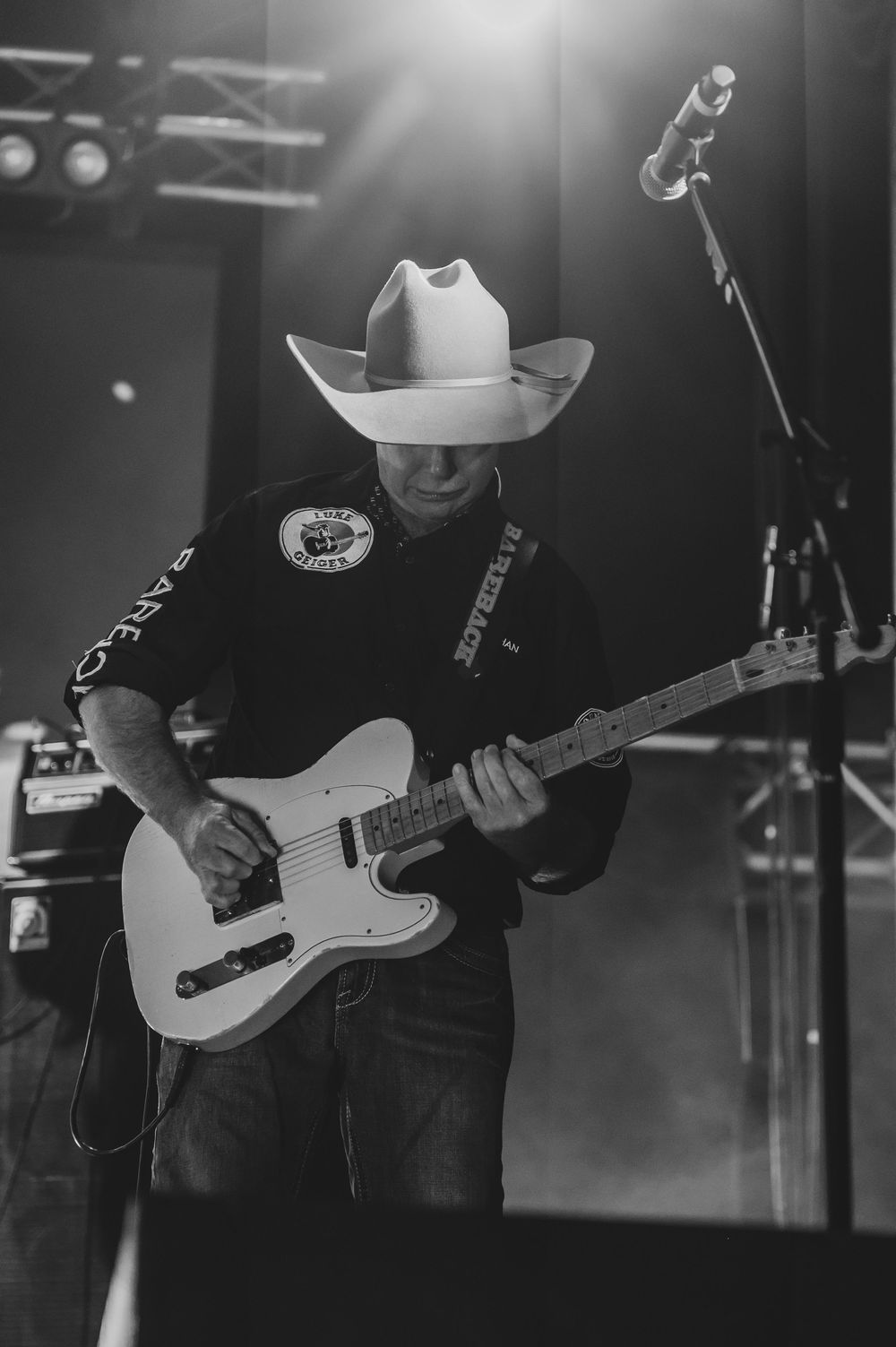 Black and white photo of a country musician in a cowboy hat playing a white Telecaster guitar on stage.