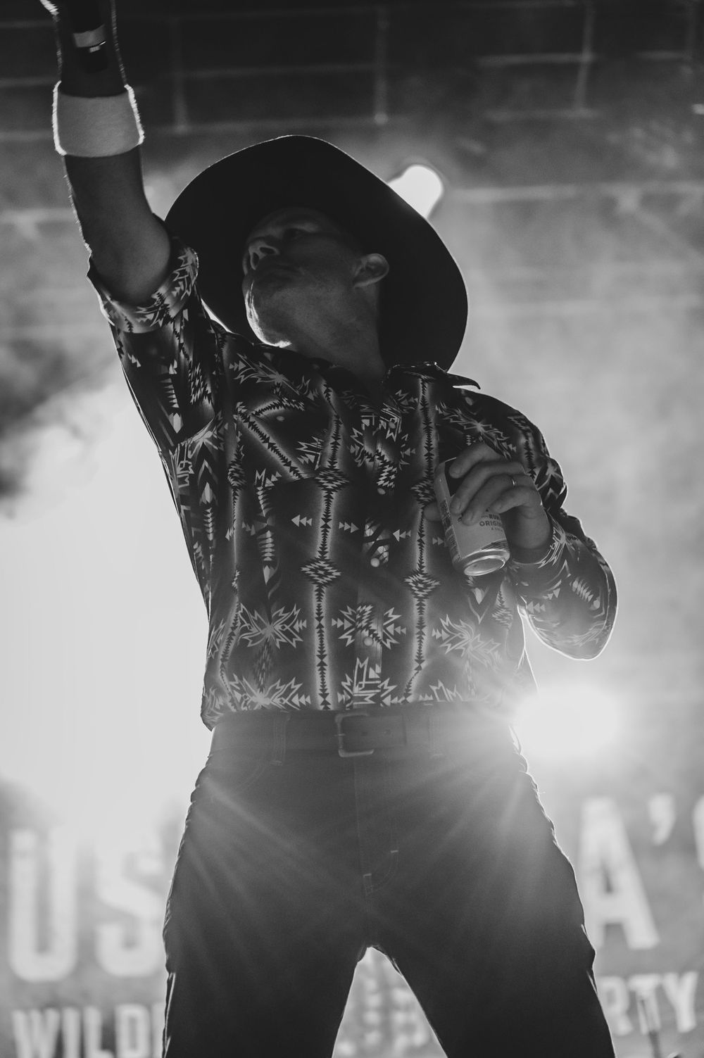 Black and white photo of a cowboy hat performer raising fist on stage with dramatic smoke and lighting effects.