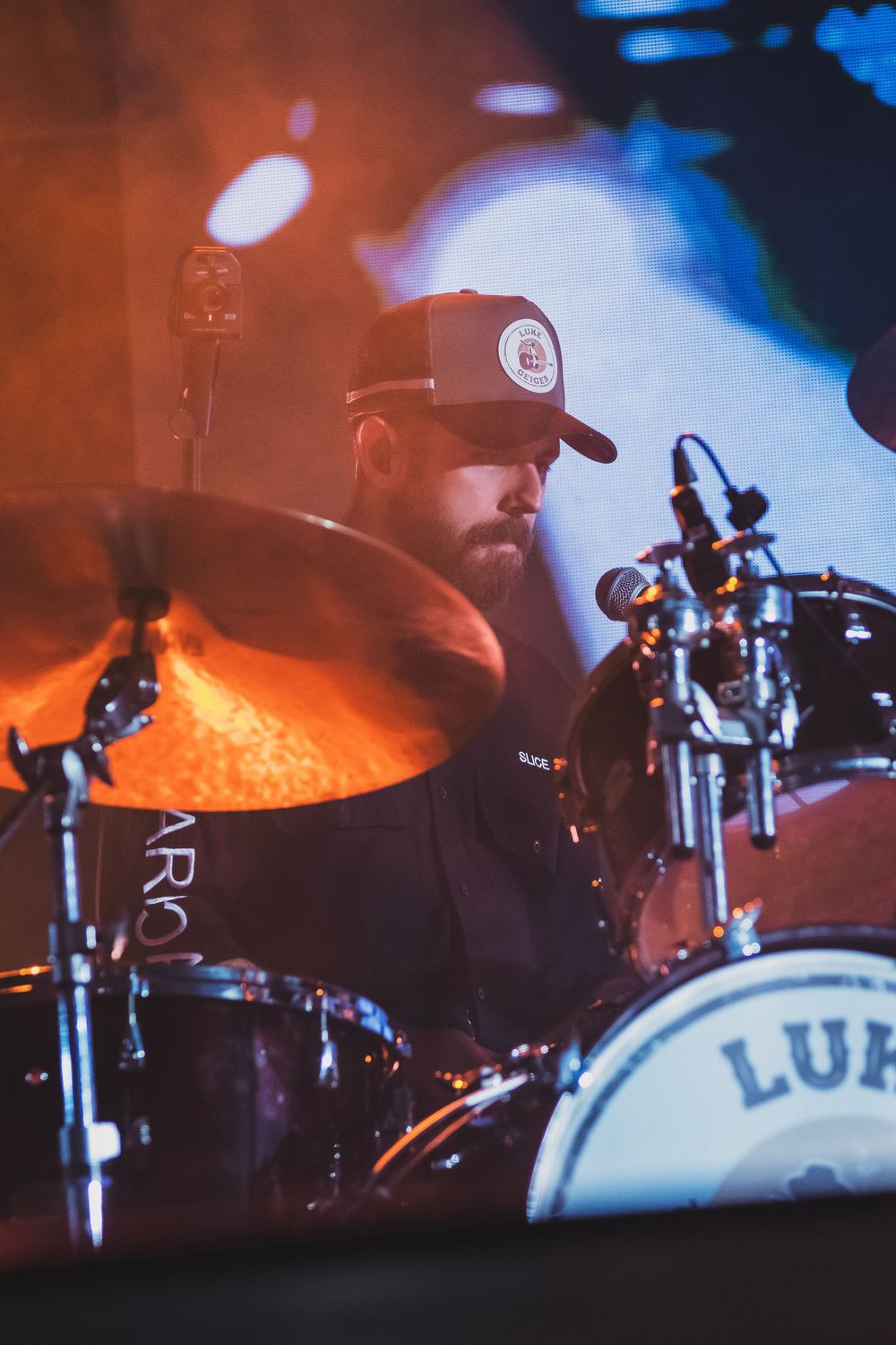 Bearded drummer performing on stage with Ludwig drum kit, cymbal glowing under warm orange stage lighting.