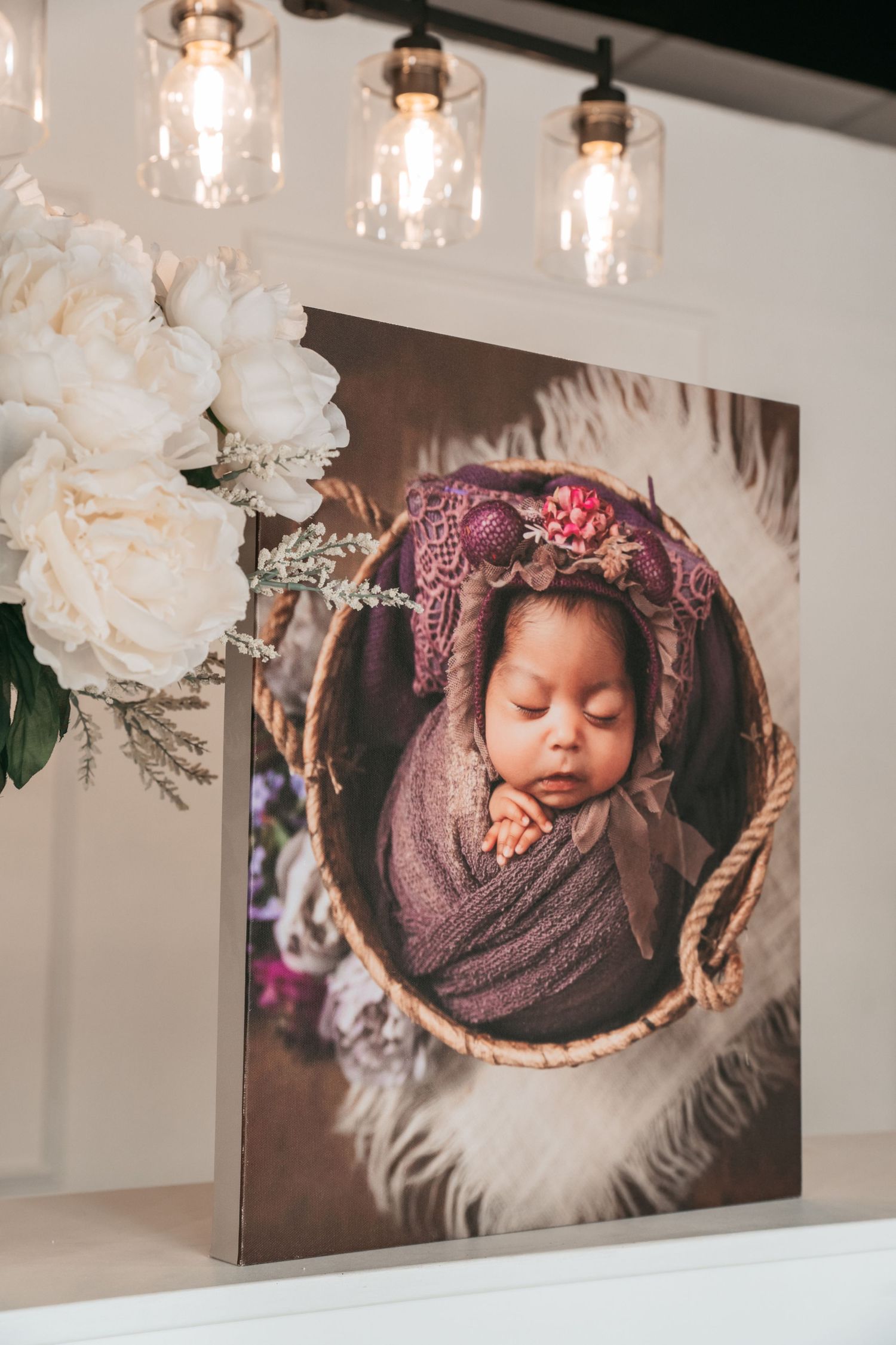 Gallery wall showcasing elegant newborn portraits with delicate lighting and white floral accents.