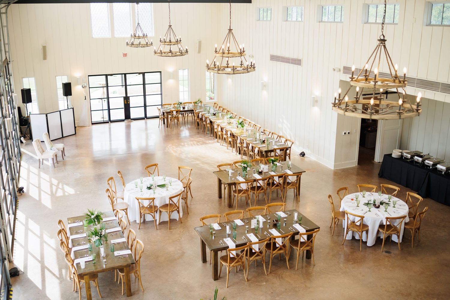 The interior of Bella Cavalli, a wedding reception venue with rustic wooden tables, white chairs, and chandeliers in a bright airy space.