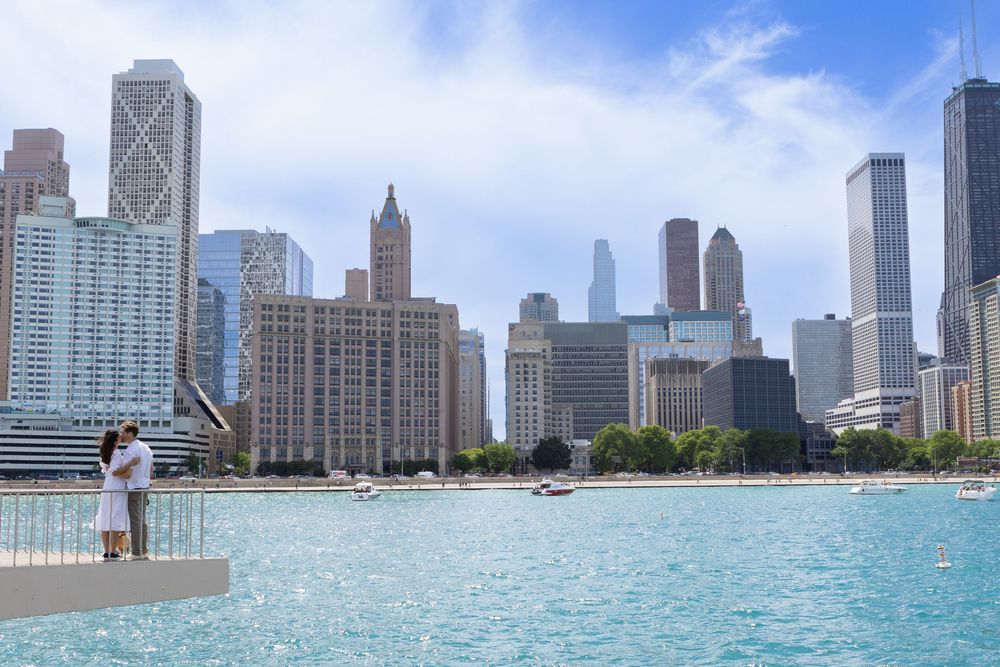 Couple embracing on Chicago lakefront with stunning city skyline and blue waters on a partly cloudy day.