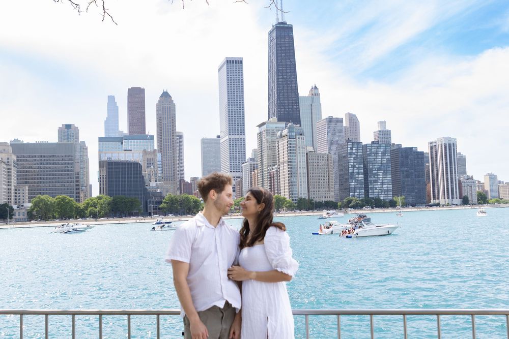 Couple posing together by Lake Michigan with Chicago skyline and John Hancock Center in background.