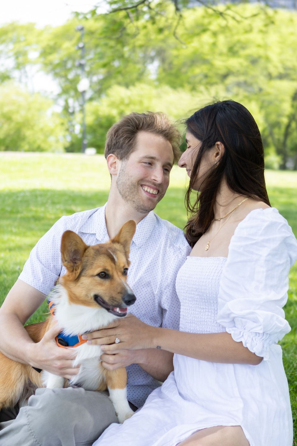 Happy couple sitting on grass in a park with their Corgi dog on a sunny day.