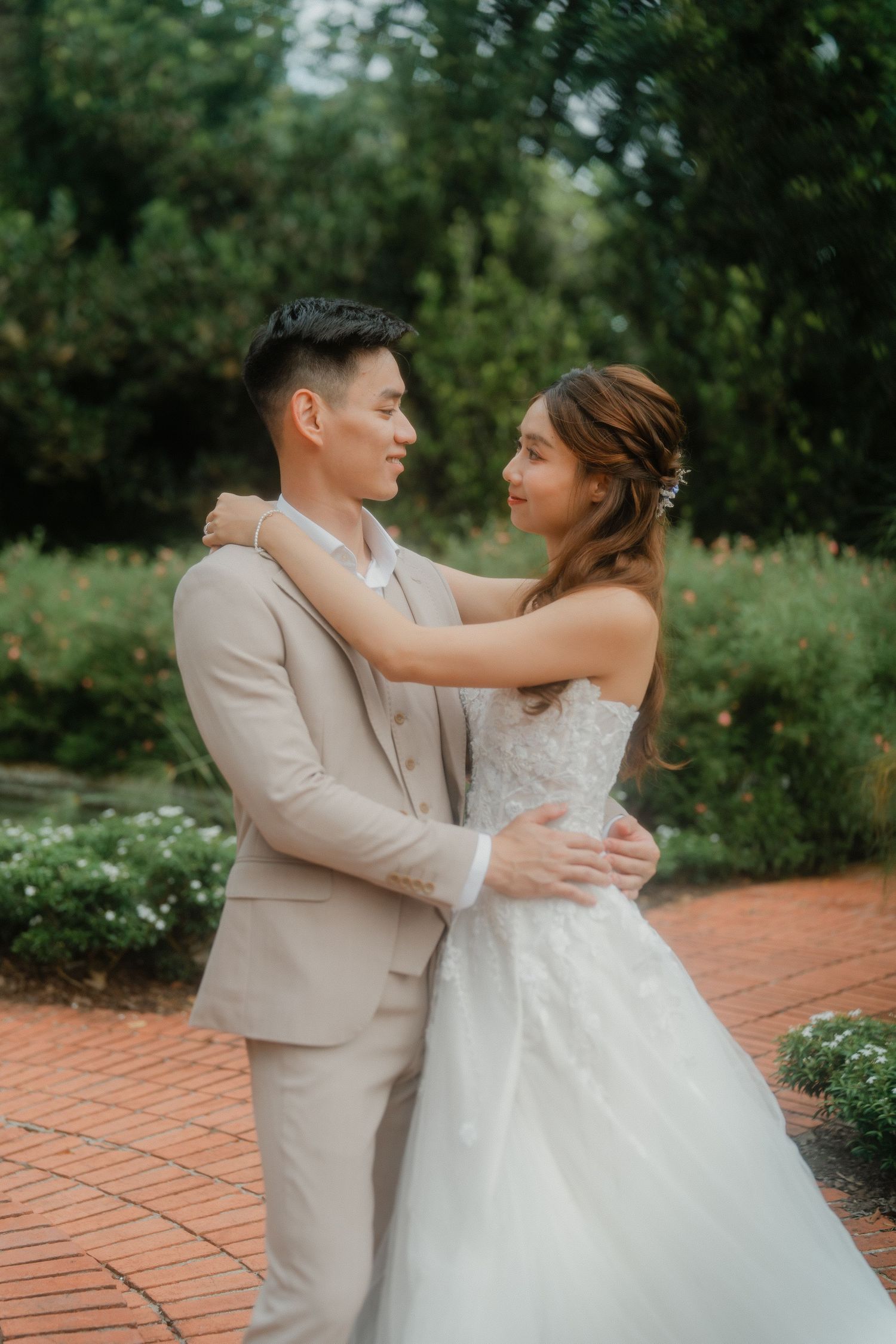 A couple shares a romantic moment on brick path surrounded by lush garden greenery.