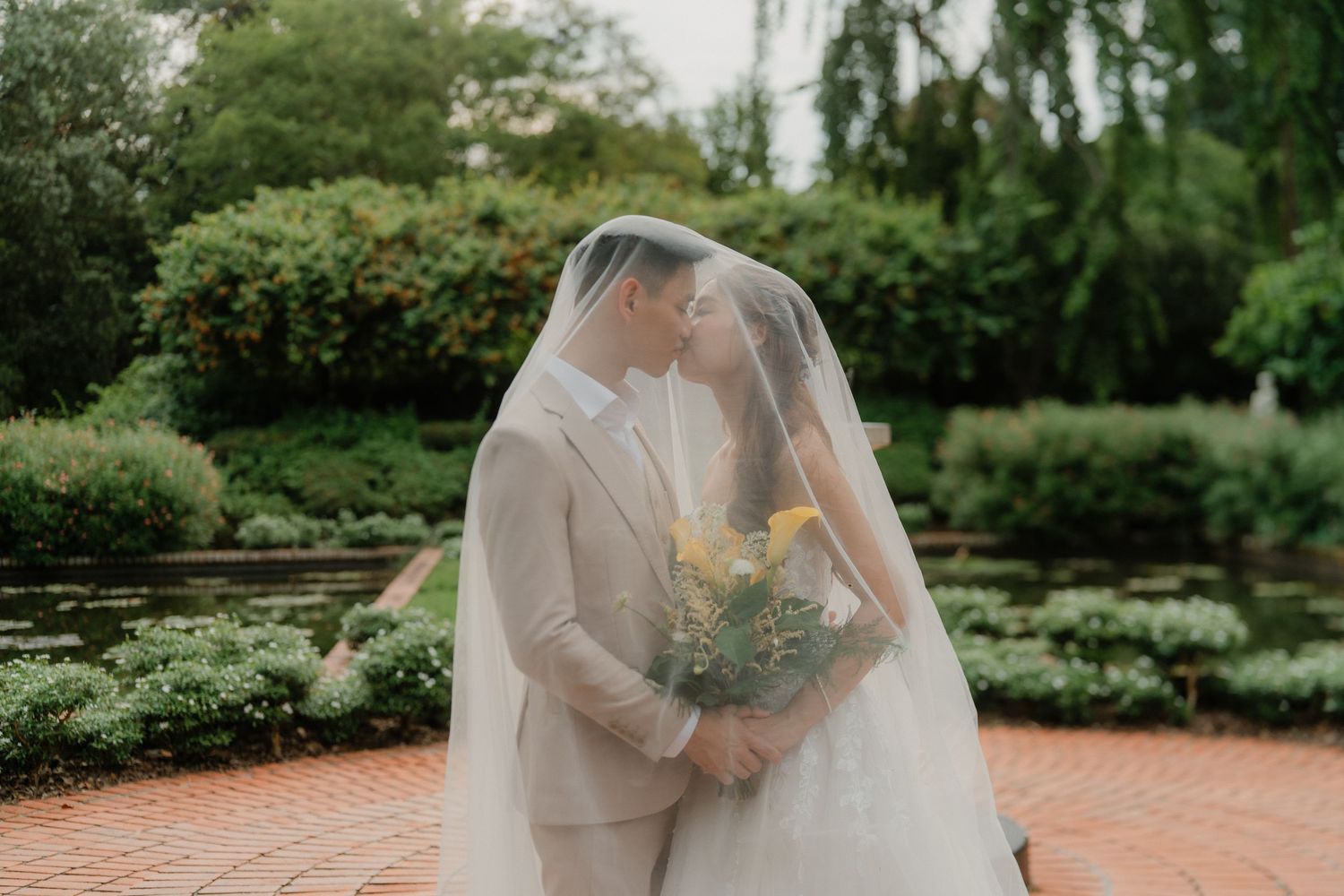 A bride and groom share an intimate pose during their wedding ceremony at a serene garden venue.