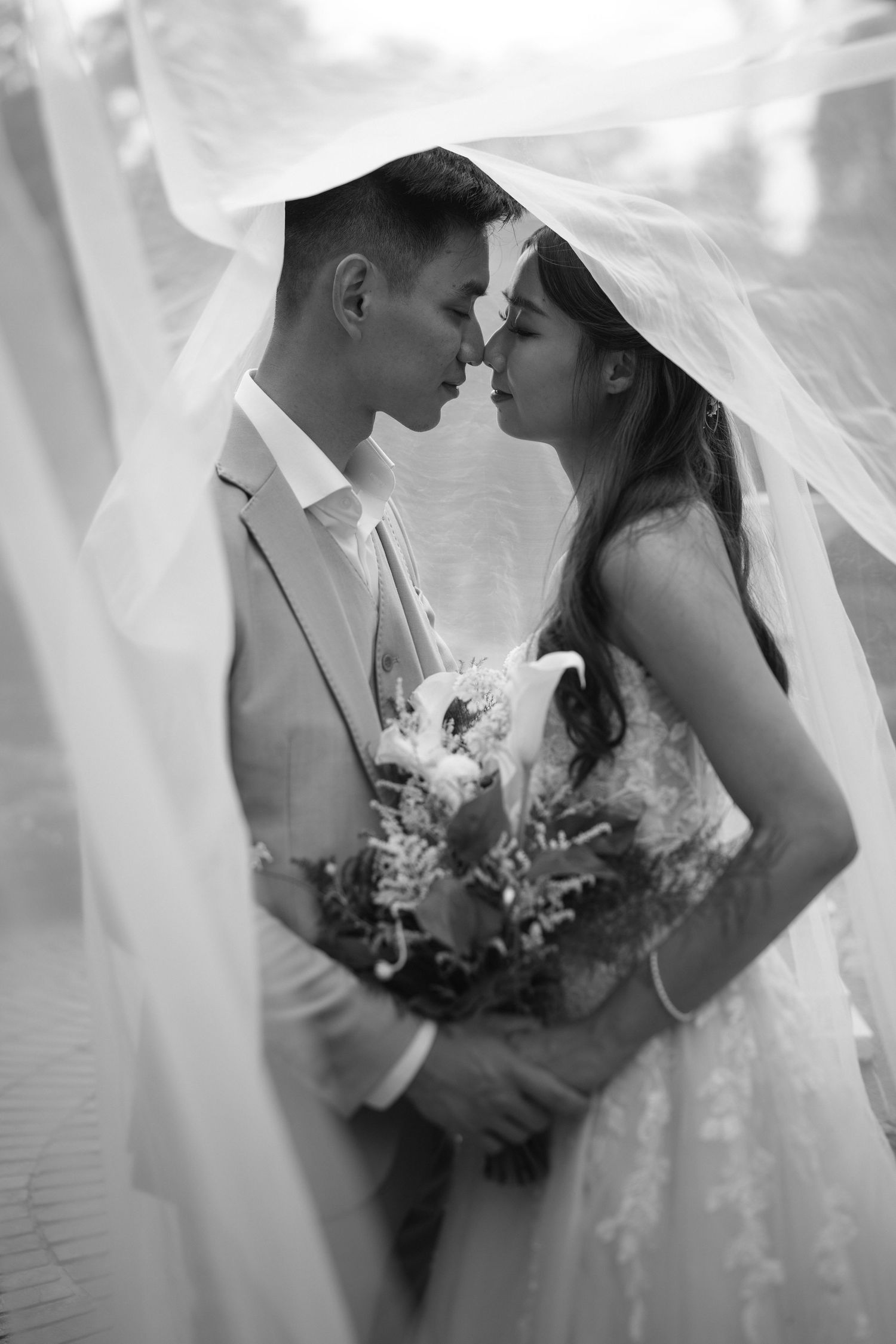 A romantic black and white wedding photo series showing intimate moments between the bride and groom through sheer fabric.