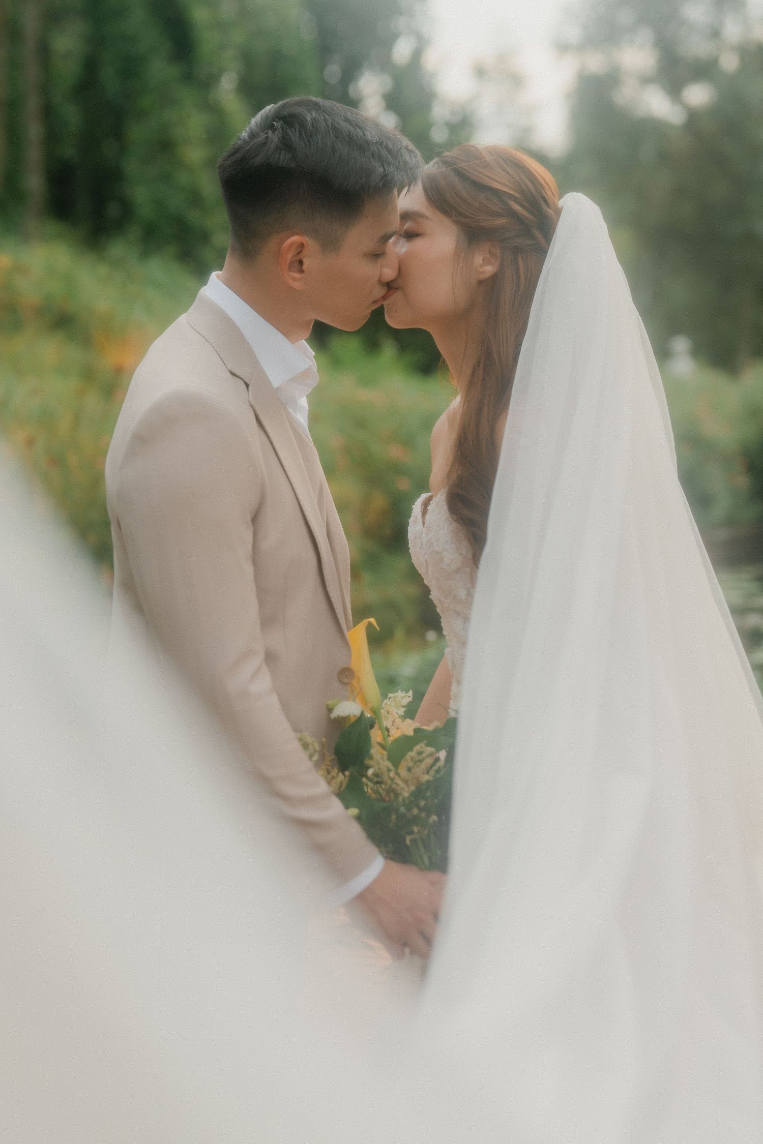 A romantic wedding couple sharing a kiss in a misty garden setting, with the bride wearing a flowing white veil.