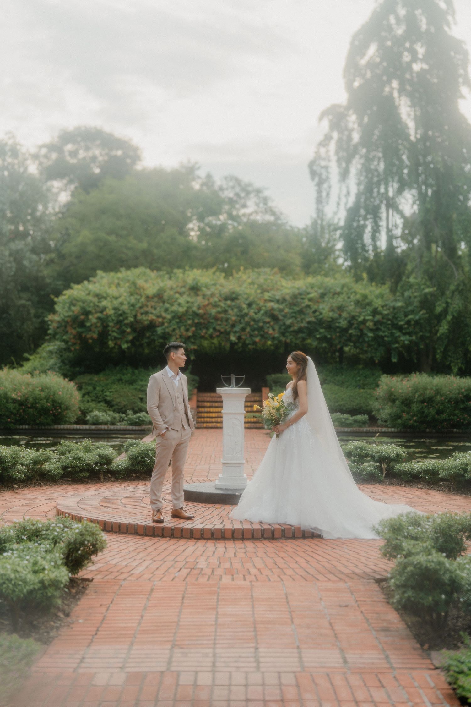Newly married couple shares a tender moment on the terrace surrounded by lush gardens at dusk.