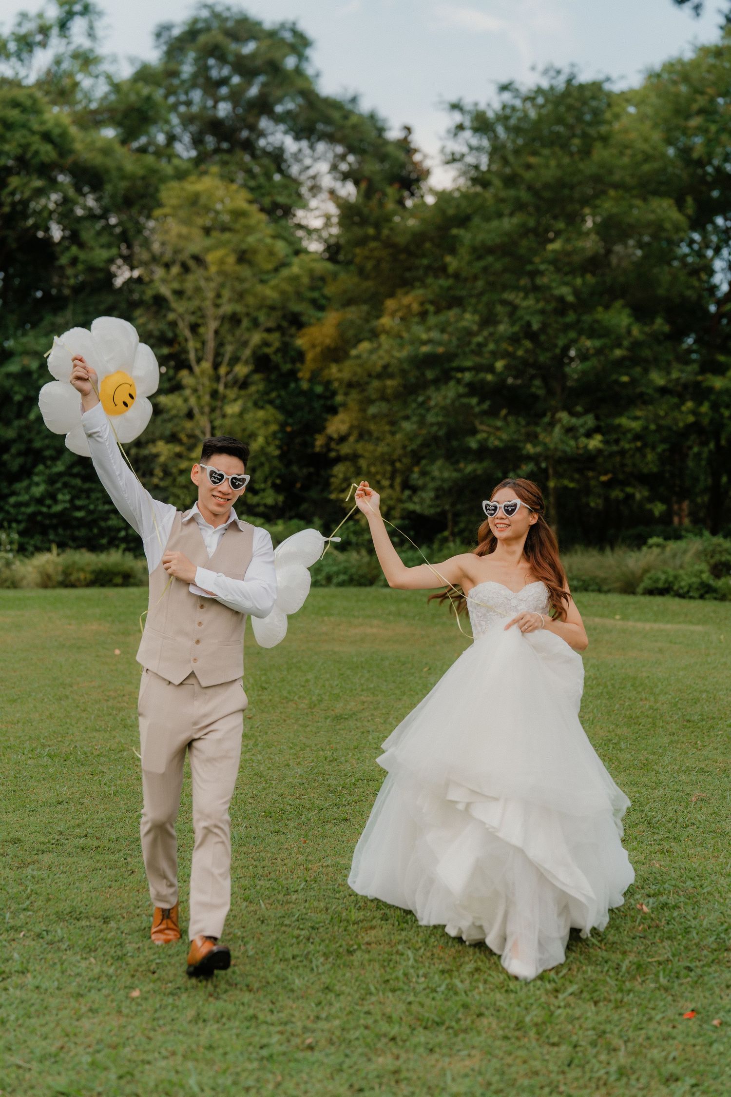 A joyful couple dances on a green lawn during a summer wedding, with the groom holding white balloons.
