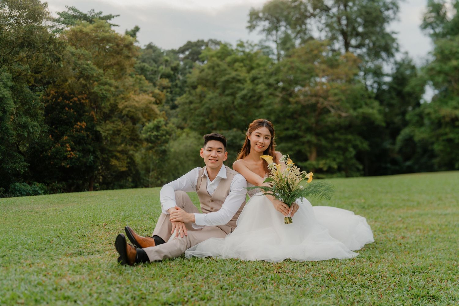 Newlyweds relaxing on grass during outdoor garden wedding photoshoot.