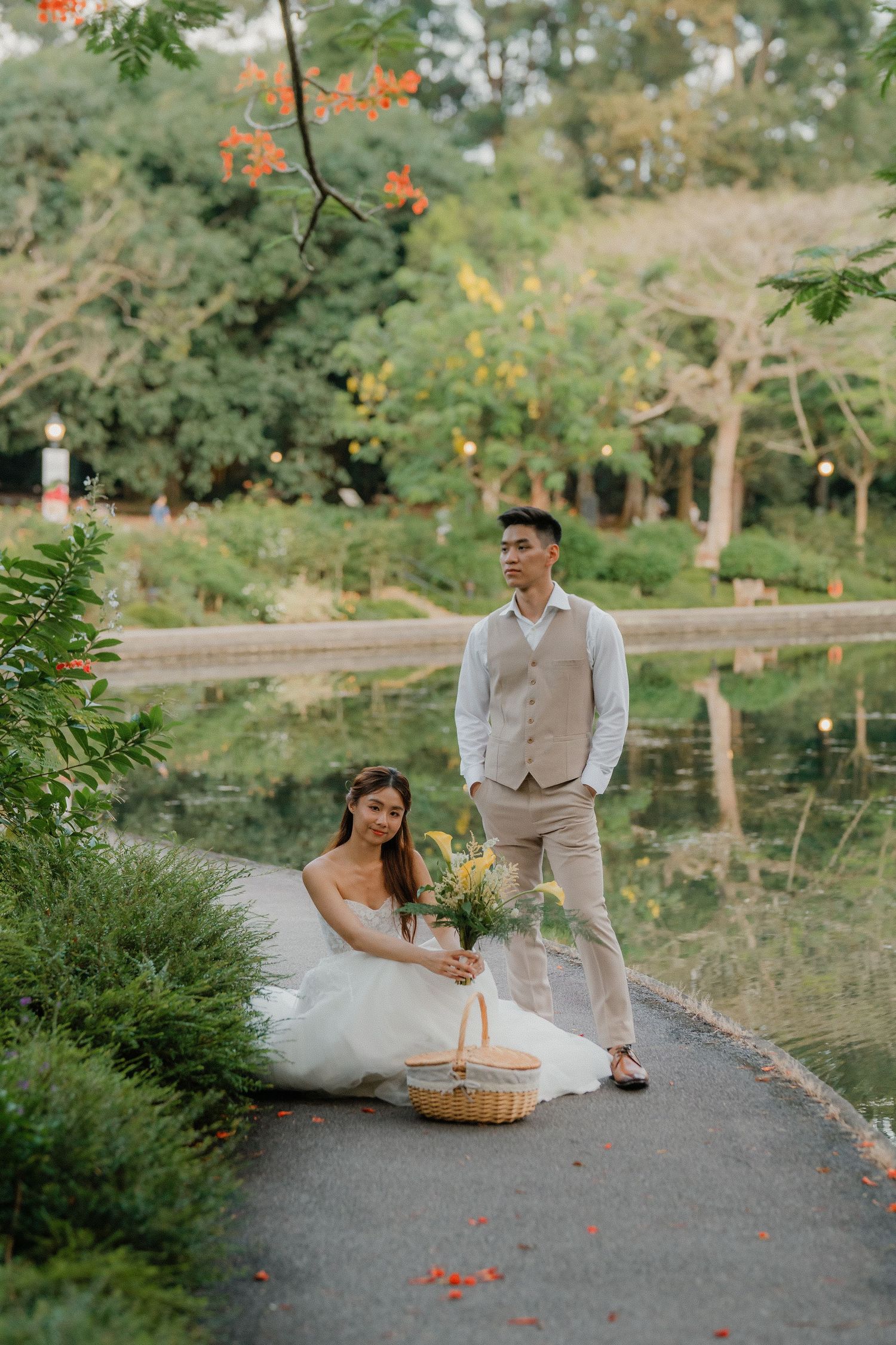 A romantic engagement photo session featuring a couple posing on a pathway near a serene pond surrounded by lush greenery.