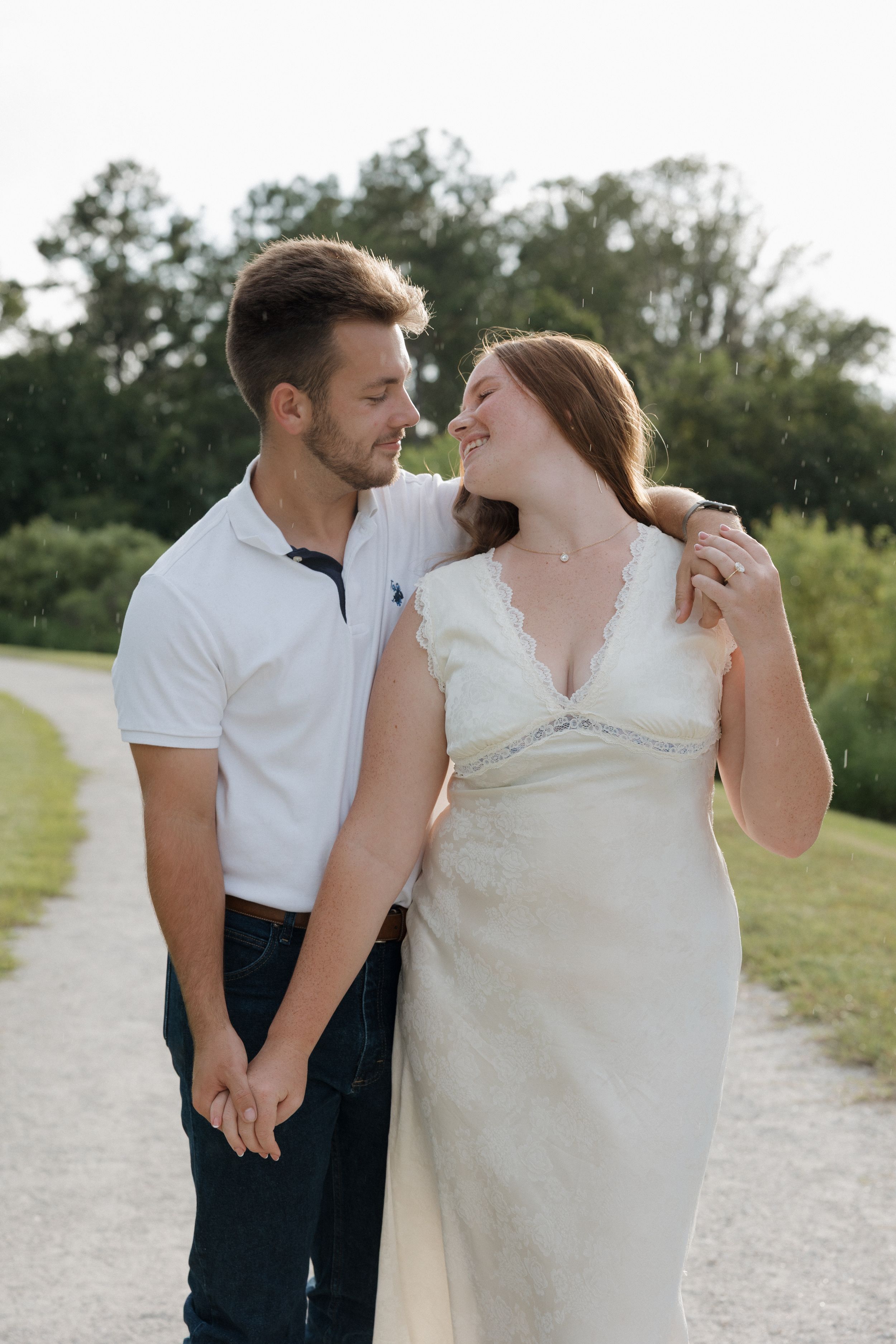 A romantic couple shares an intimate moment on a gravel path surrounded by greenery.