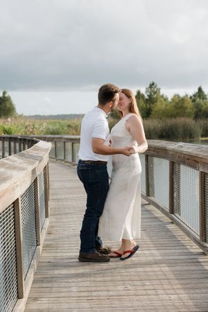 A couple in coordinating white outfits shares a tender moment on a wooden boardwalk.