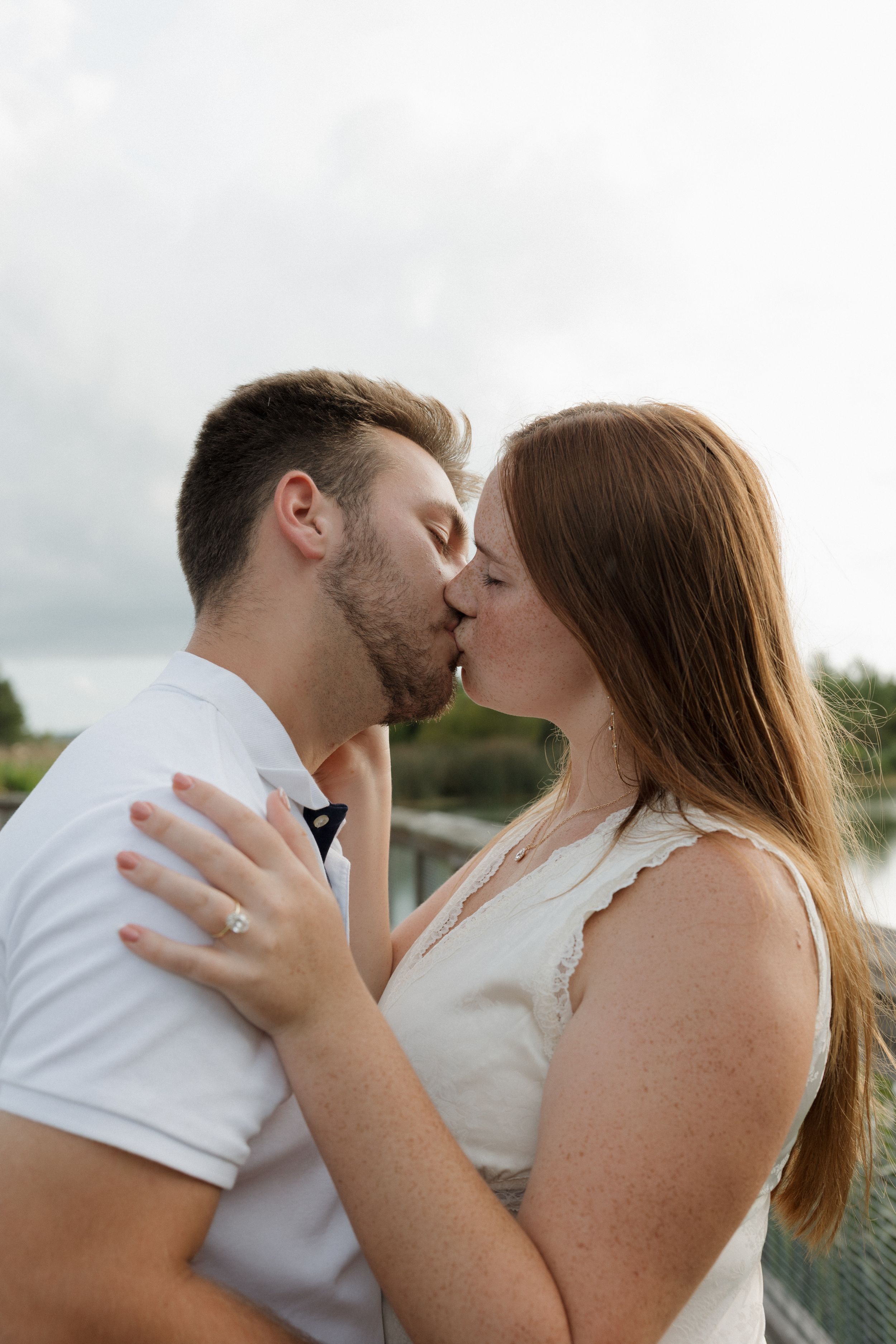 A romantic couple shares a kiss against a cloudy sky background.
