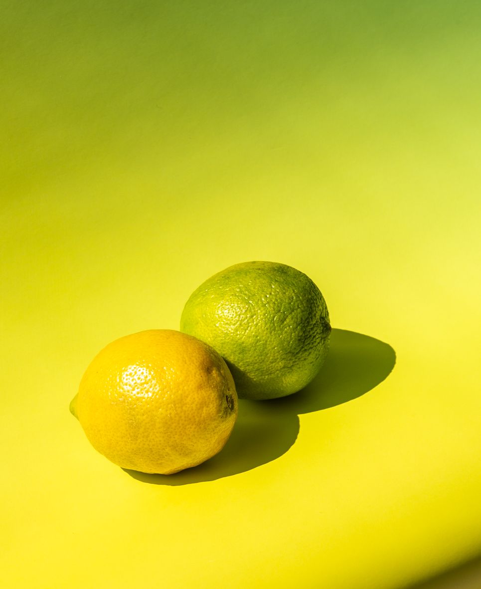Fresh yellow lemon and green lime fruits casting shadows on bright yellow background.