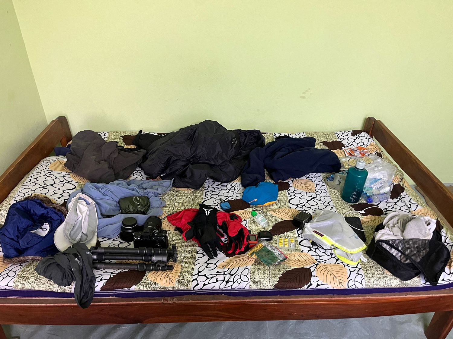 Messy bed covered with scattered clothes and personal items in a long panoramic view.