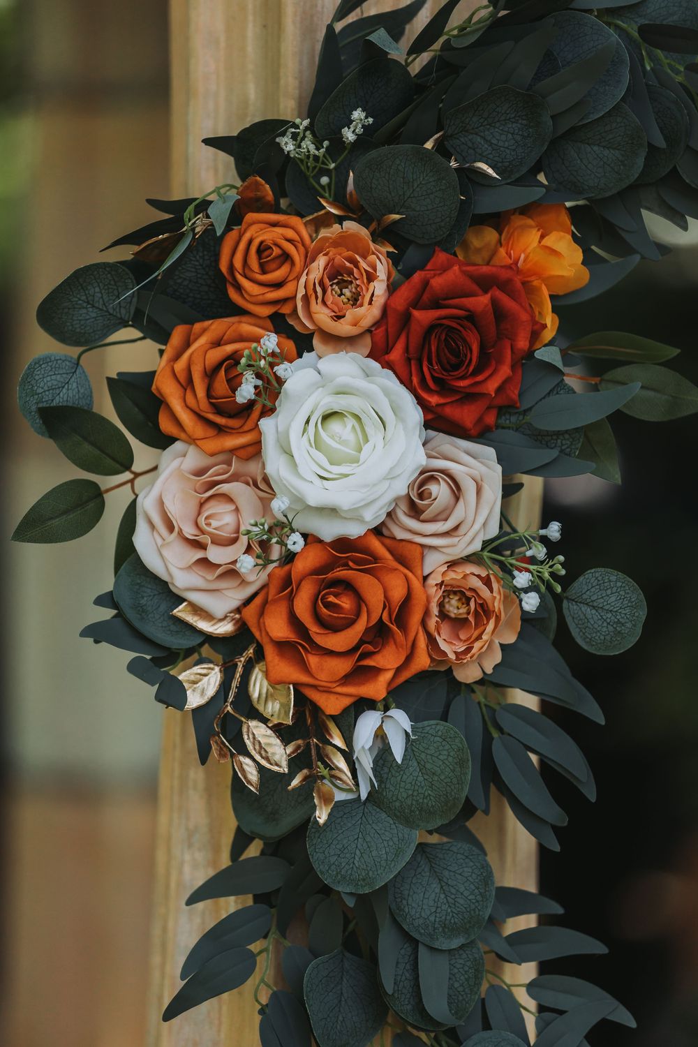 Beautiful floral arrangement featuring orange, red, pink and white roses with dark green eucalyptus leaves.