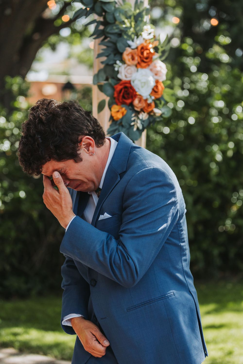 An emotional outdoor wedding moment captured at a ceremony site decorated with orange and white floral arrangements.