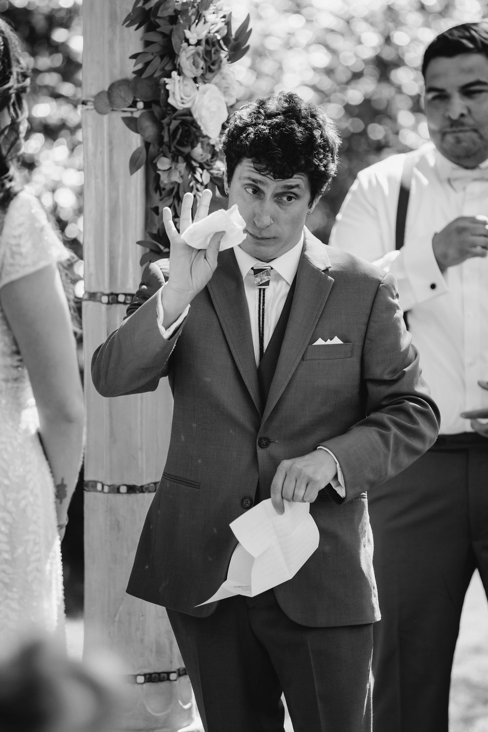 A montage of four black and white photos showing a person in a dark suit waving and interacting with others outdoors.