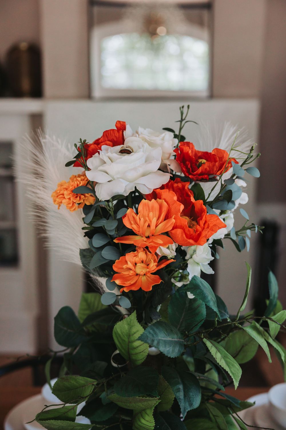 A vibrant floral arrangement featuring red, orange and white blooms with dark green foliage in soft indoor lighting.
