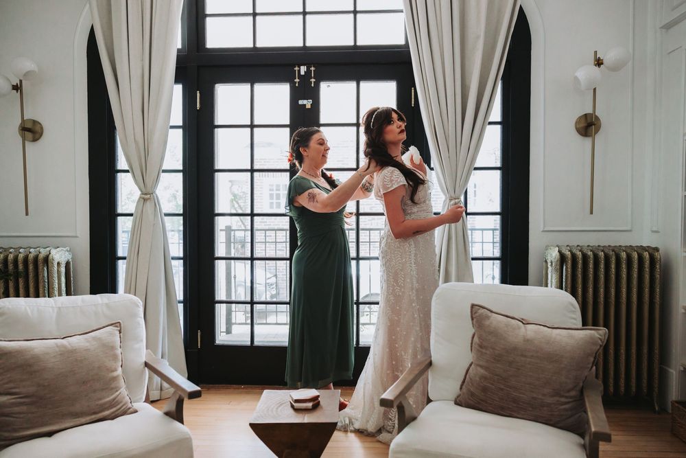 Two people prepare for a special occasion in a bright room with white curtains and upholstered furniture.