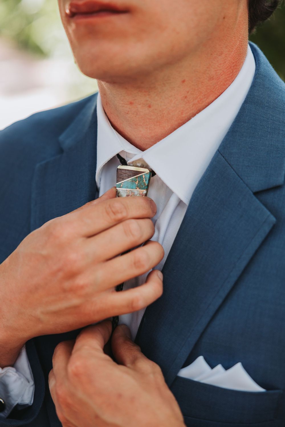 Close-up of a groom adjusting his tie while wearing a navy blue suit with white pocket square.