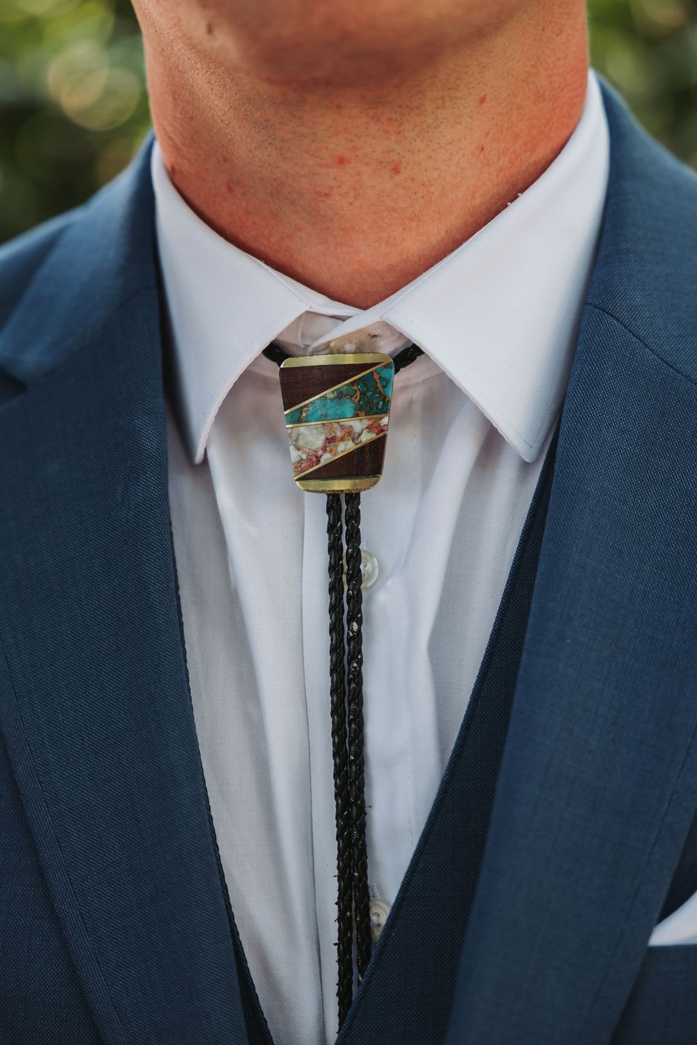 Close-up of a navy suit with white dress shirt and southwestern style bolo tie featuring turquoise stone detail.