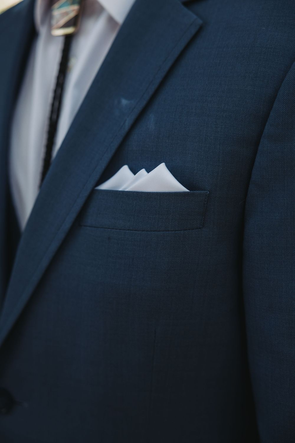 A row of navy blue groomsmen suits with white pocket squares showing formal wedding attire details.
