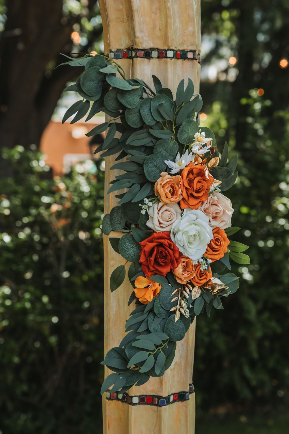 Beautiful floral arrangement with orange and white roses mixed with eucalyptus leaves decorating a wooden post.