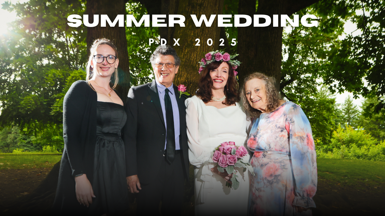 A row of well-dressed wedding guests standing outside in a wooded outdoor garden setting.