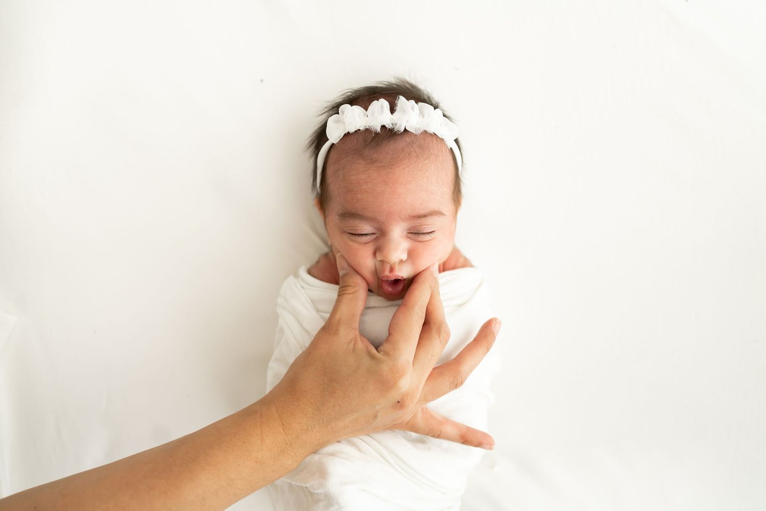 Newborn baby wrapped in soft white knit blanket with tan bow sleeping peacefully.