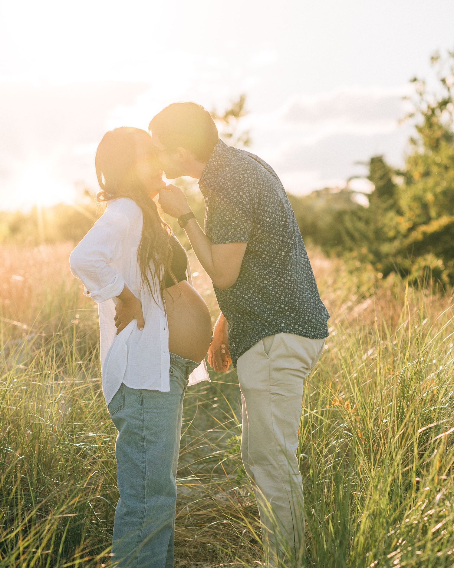 A couple shares a tender moment in tall grass during golden hour.