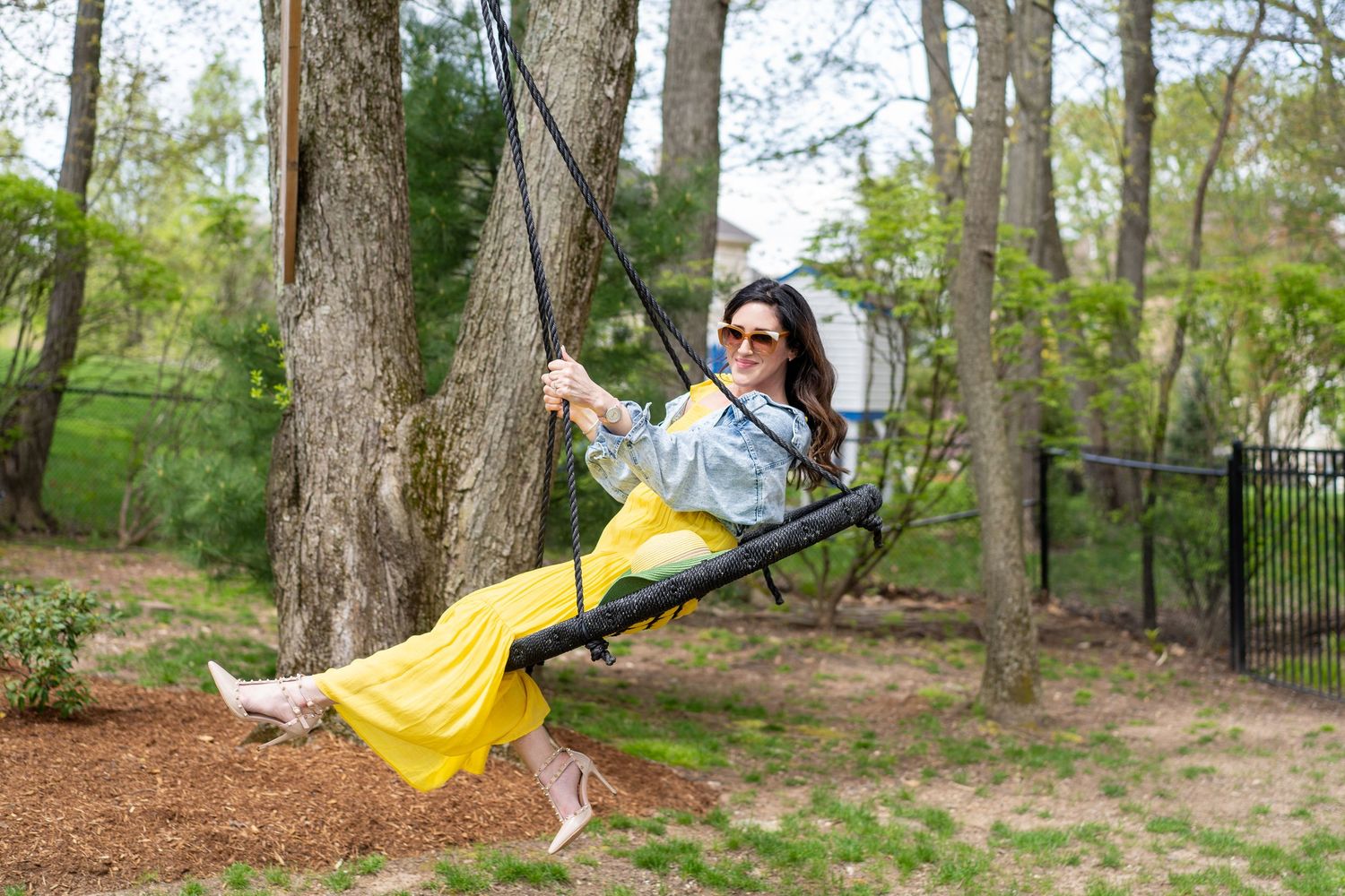 Person wearing yellow dress swinging joyfully in wooded park setting.