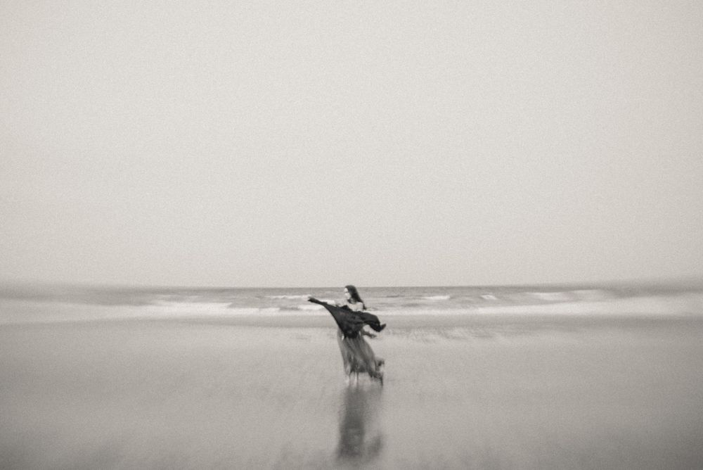 A silhouetted figure dances against a misty beach horizon in black and white.