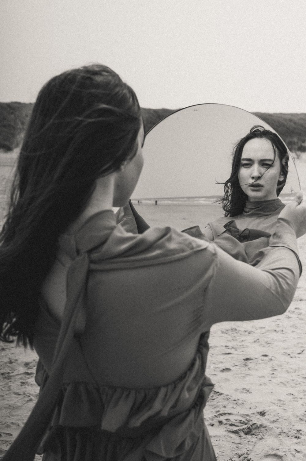 A series of artistic mirror reflections show a figure against a moody beach landscape.