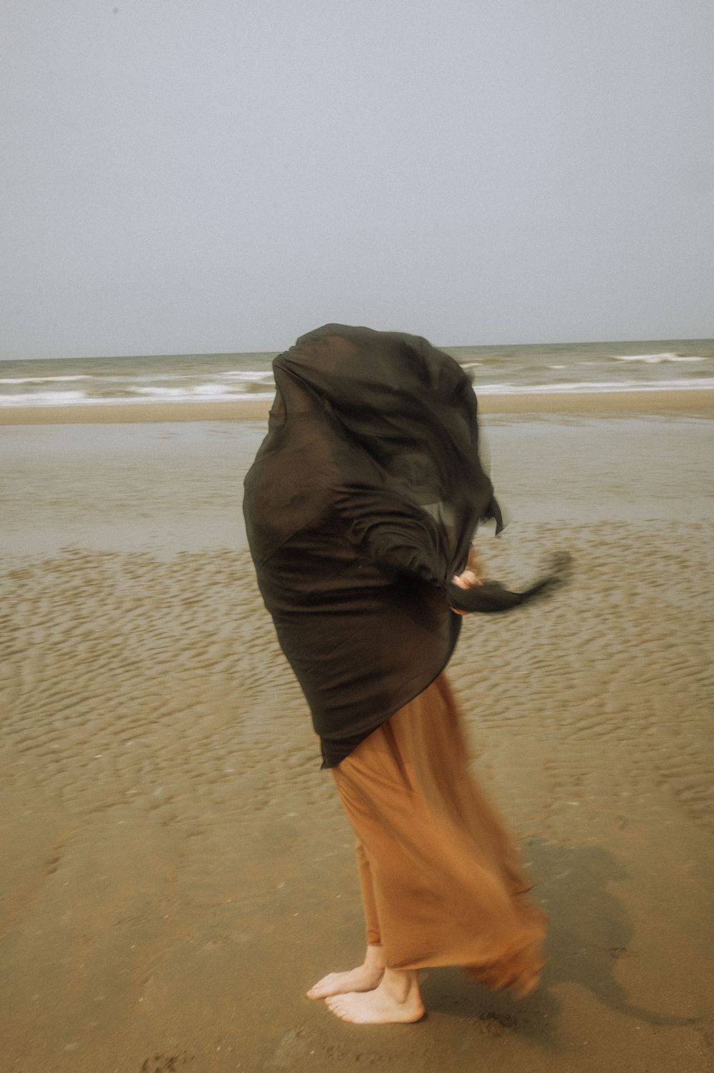 A figure in dark clothing moves dramatically against a windswept beach backdrop.