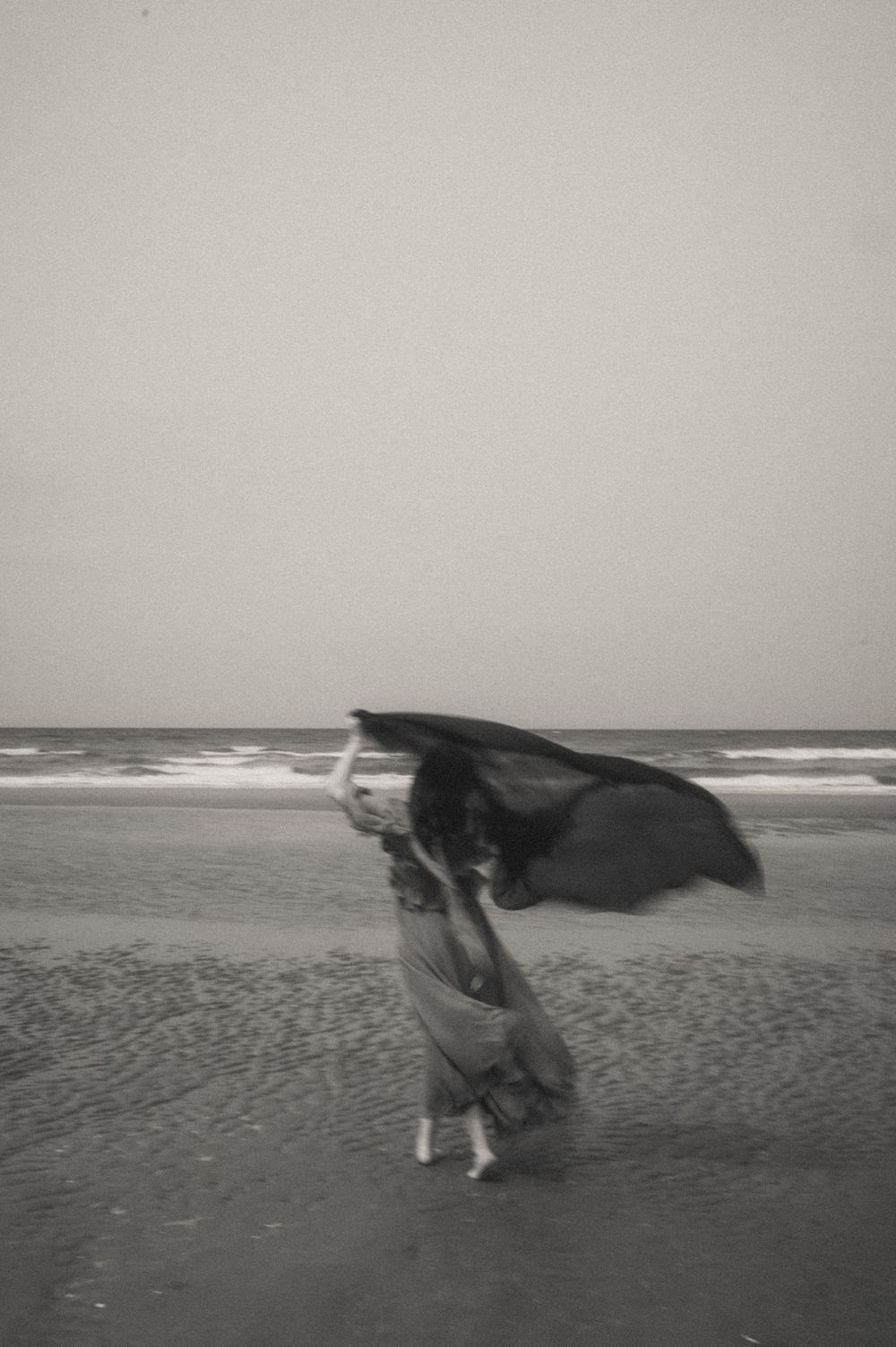A dramatic black and white scene of fabric flowing in the wind on a beach.