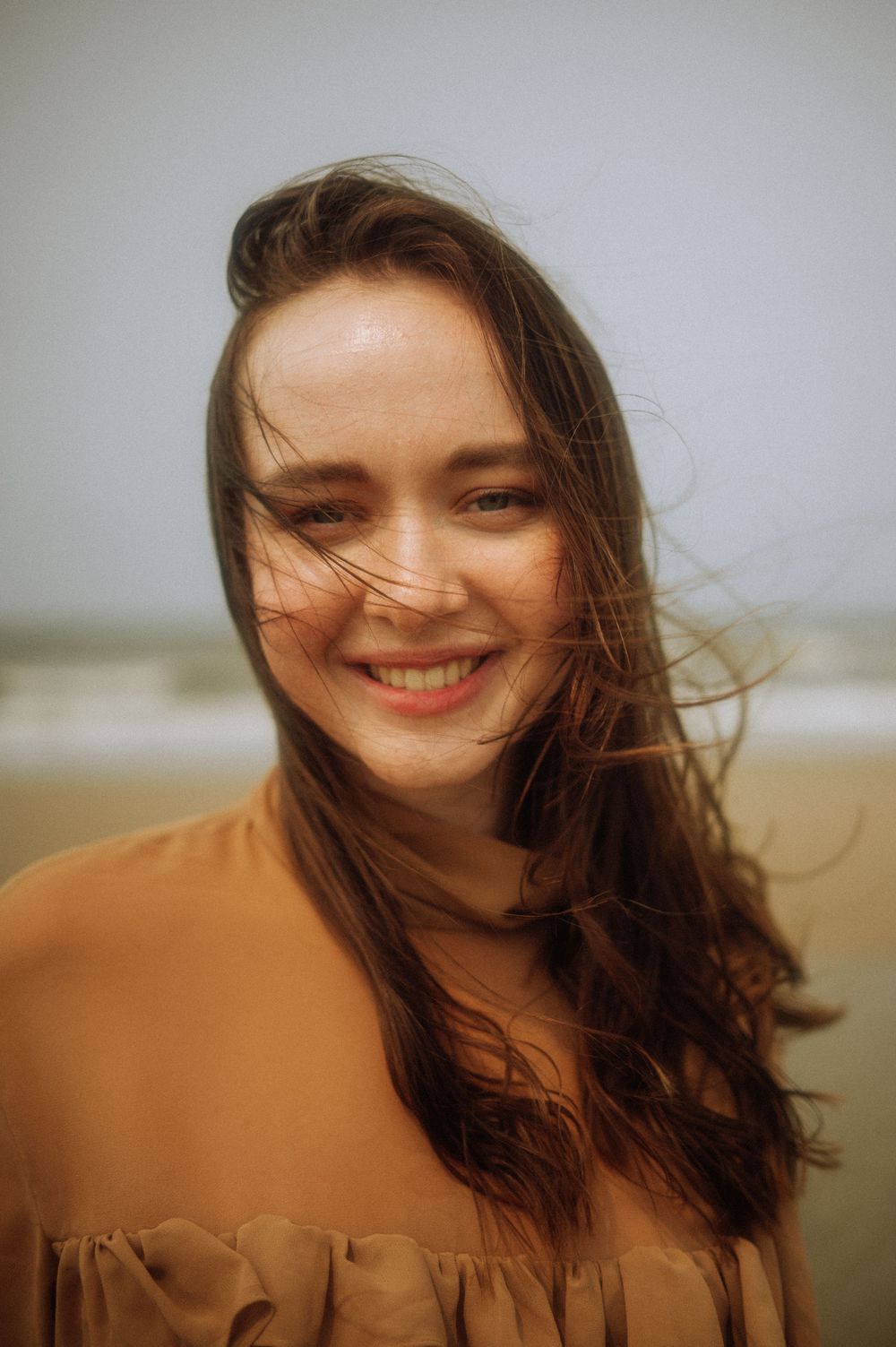 A warm-toned portrait captures windswept hair against a soft background.