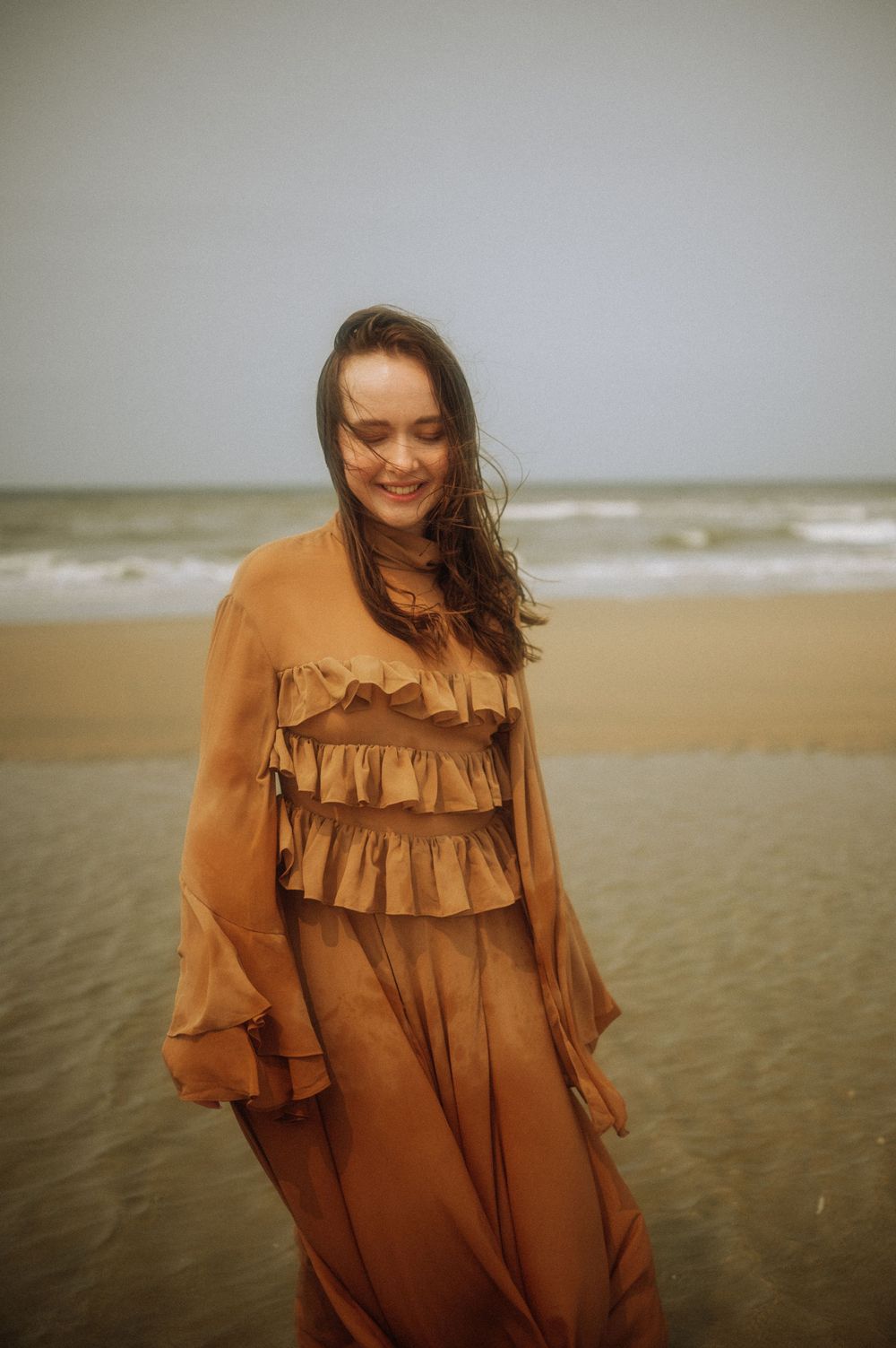A ruffled brown dress catches the wind on a moody beach landscape.