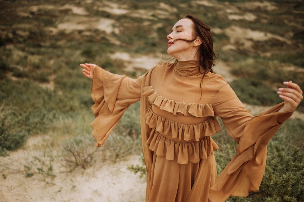 A figure in a flowing dress moves gracefully against green coastal vegetation.