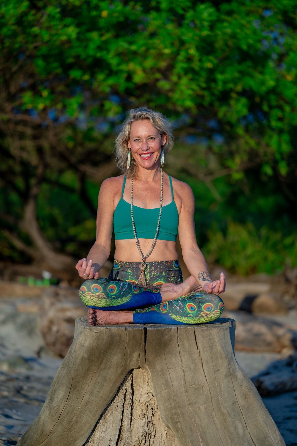 A meditation scene showing someone in a teal top sitting cross-legged on a tree stump in a peaceful outdoor setting.
